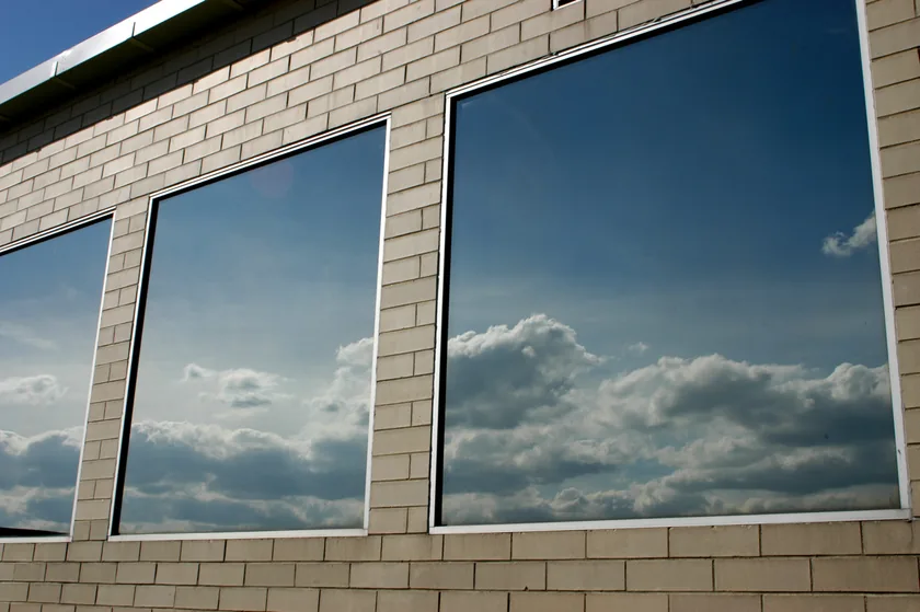 Reflective solar control window film on a commercial building's windows, mirroring the sky and clouds