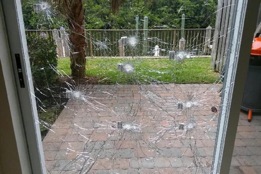 A sliding glass patio door struck in several places, cracks radiating from each impact point, the pane still whole and held in its frame with the patio visible through it